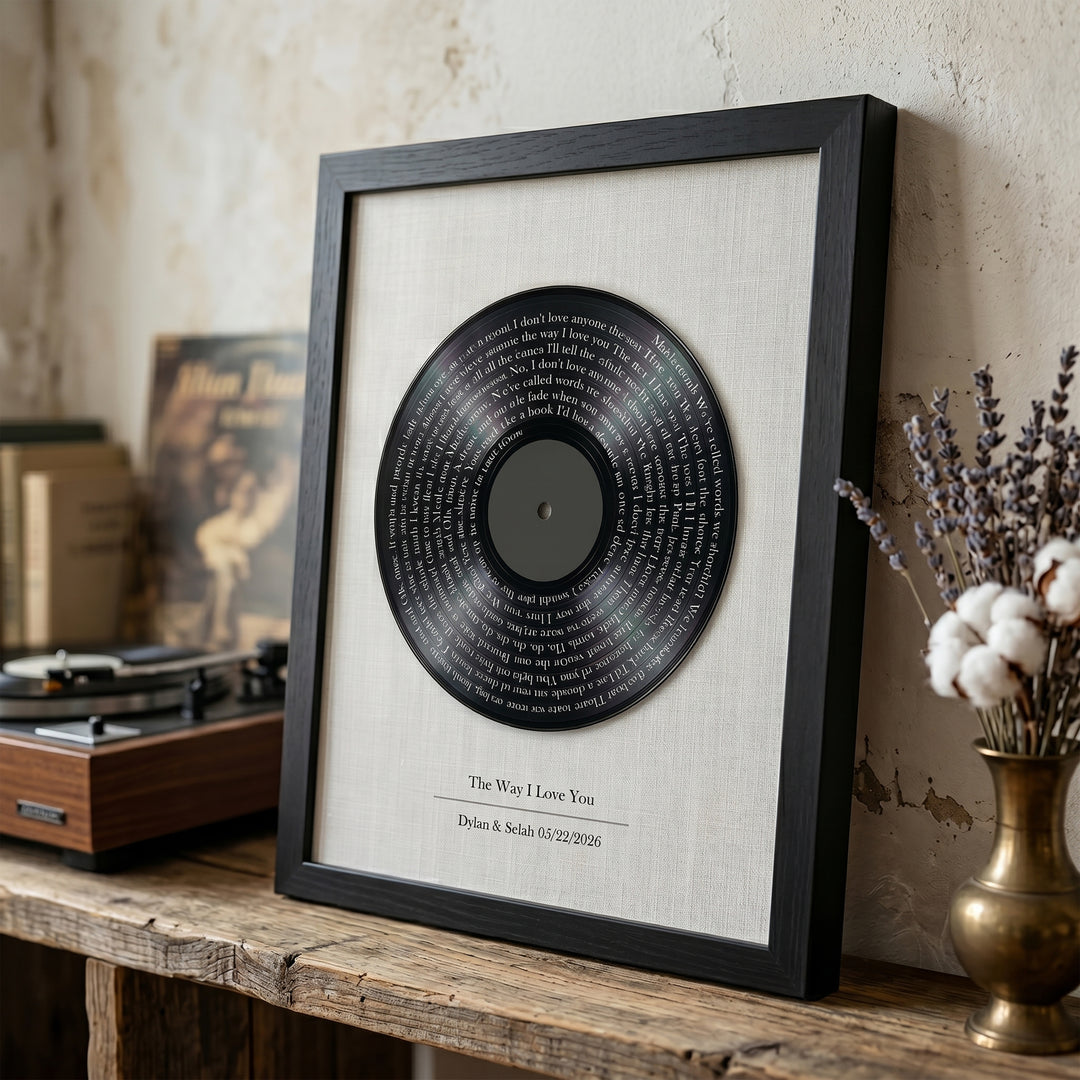 Framed vinyl record with lyrics on a wooden surface with a turntable and decorative items.