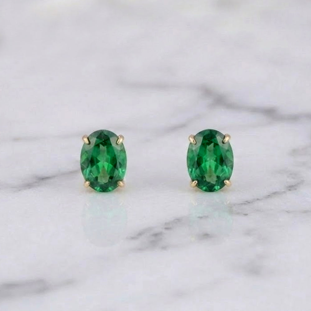 Pair of emerald gemstone stud earrings on a marble background