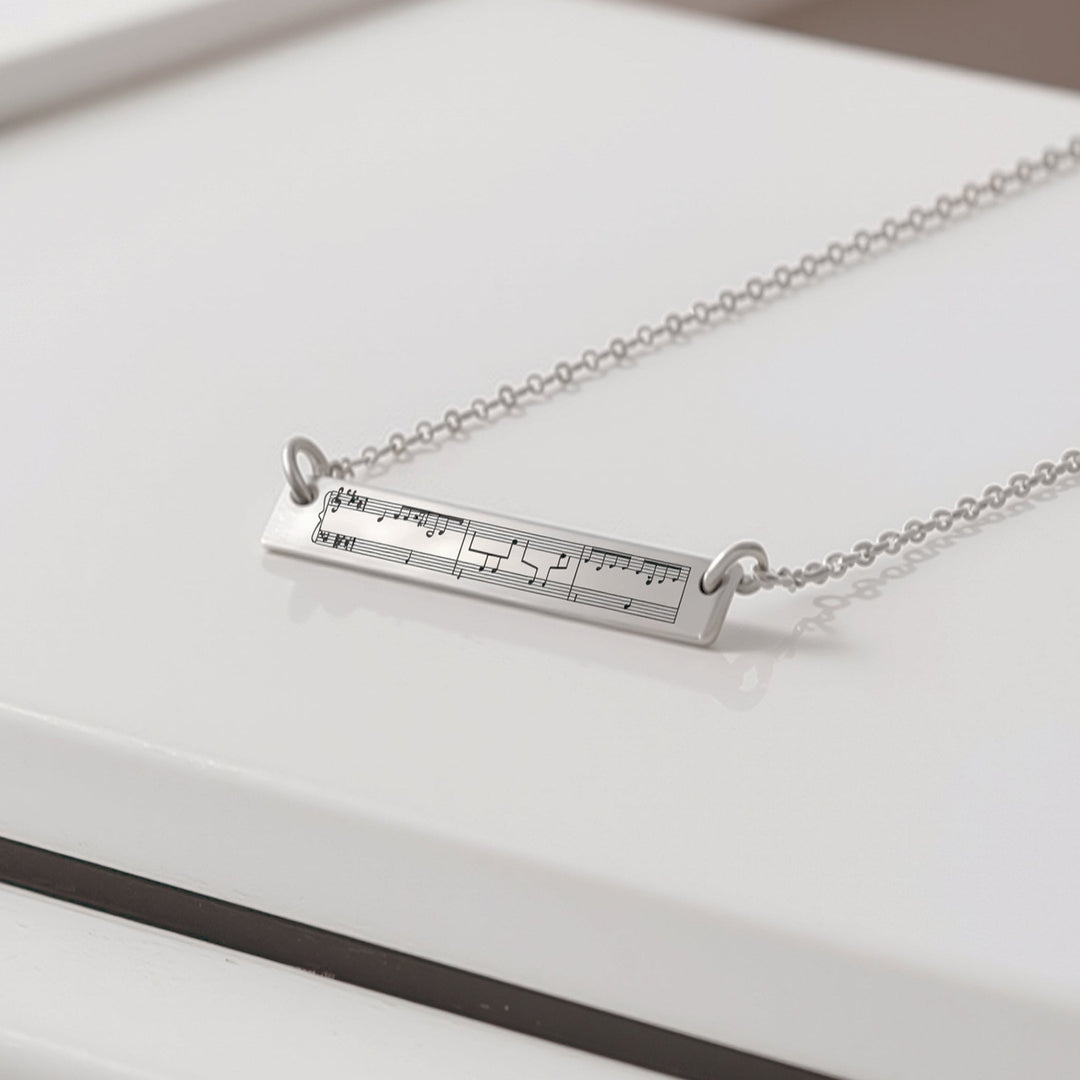 Silver necklace with engraved sheet music on top of a piano