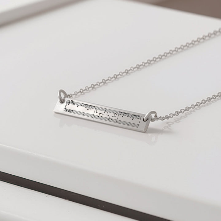 Silver necklace with engraved sheet music on top of a piano