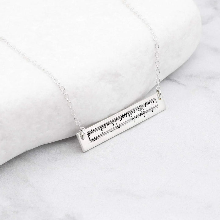 Silver necklace with a sheet music pendant featuring musical notes on a marble surface